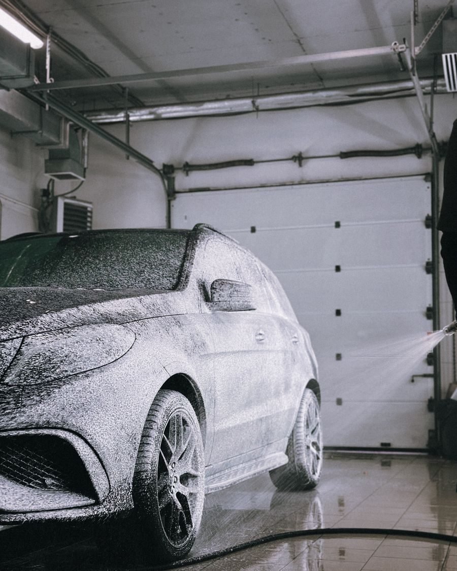 Car covered head to toe in thick wash foam inside a lit bay