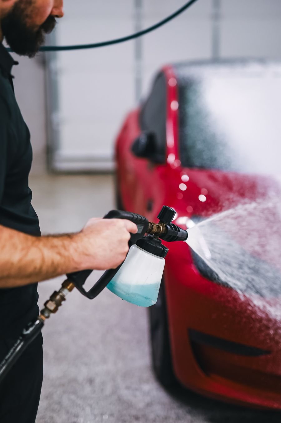 Technician spraying foam onto a red car with a pressure lance