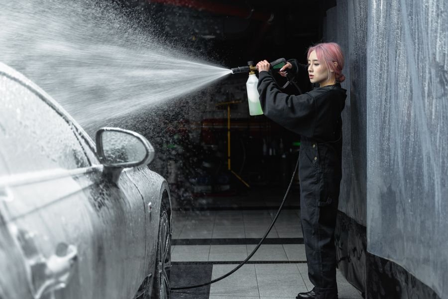 Technician pressure rinsing a foamed car in the wash bay
